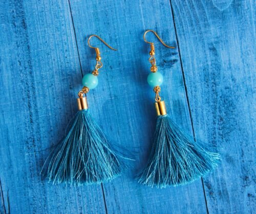 Stylish blue tassel earrings with gold accents displayed on a wooden surface.