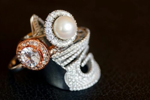 Close-up of luxurious pearl and diamond rings with gold accents on a black background.